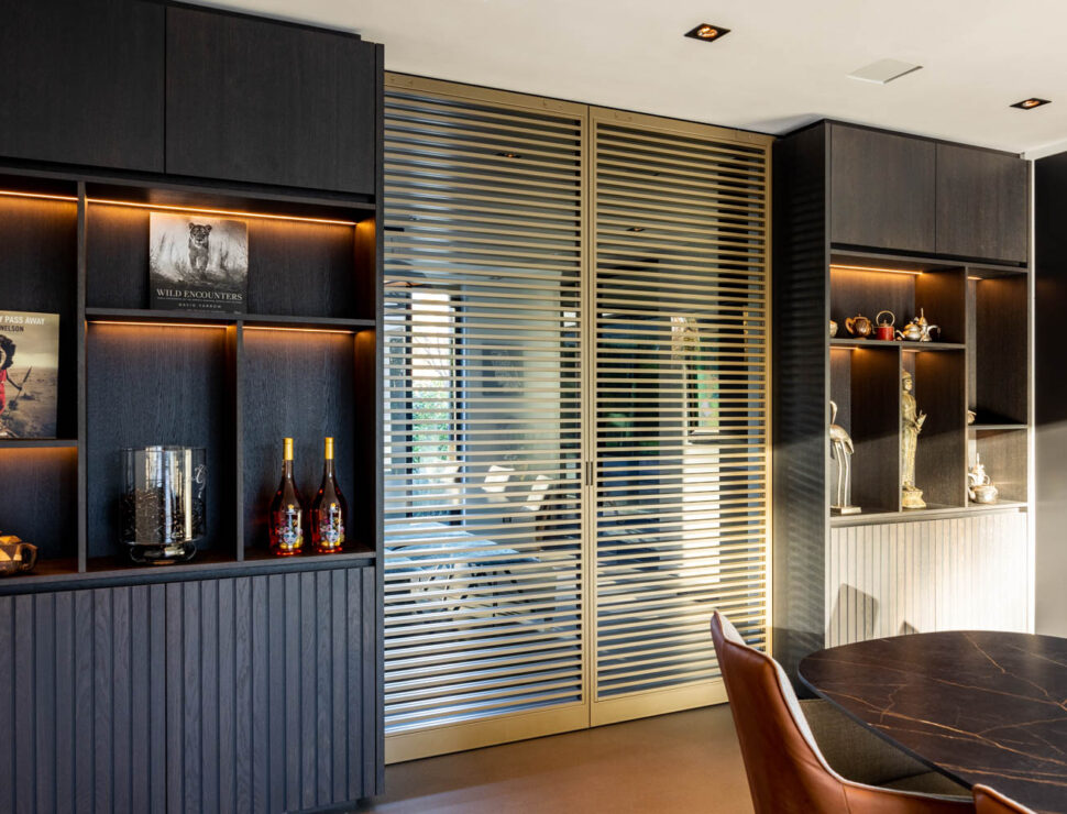 Stijlvolle Anodic Bronze stalen schuifdeuren met glas en horizontale lamellen in een luxe interieur met donkere houten kasten.